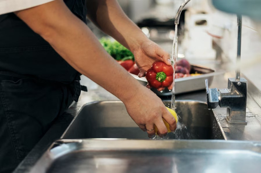 Man washing tomato on stainless steel bench